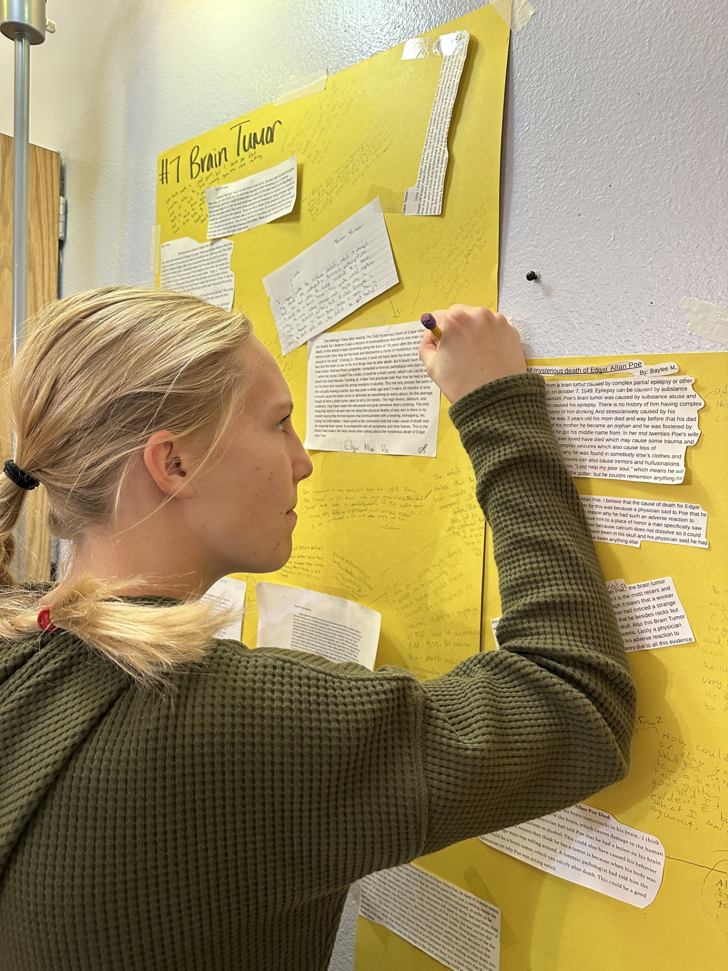 Middle School English student writing paragraph arguments on poster placed on wall