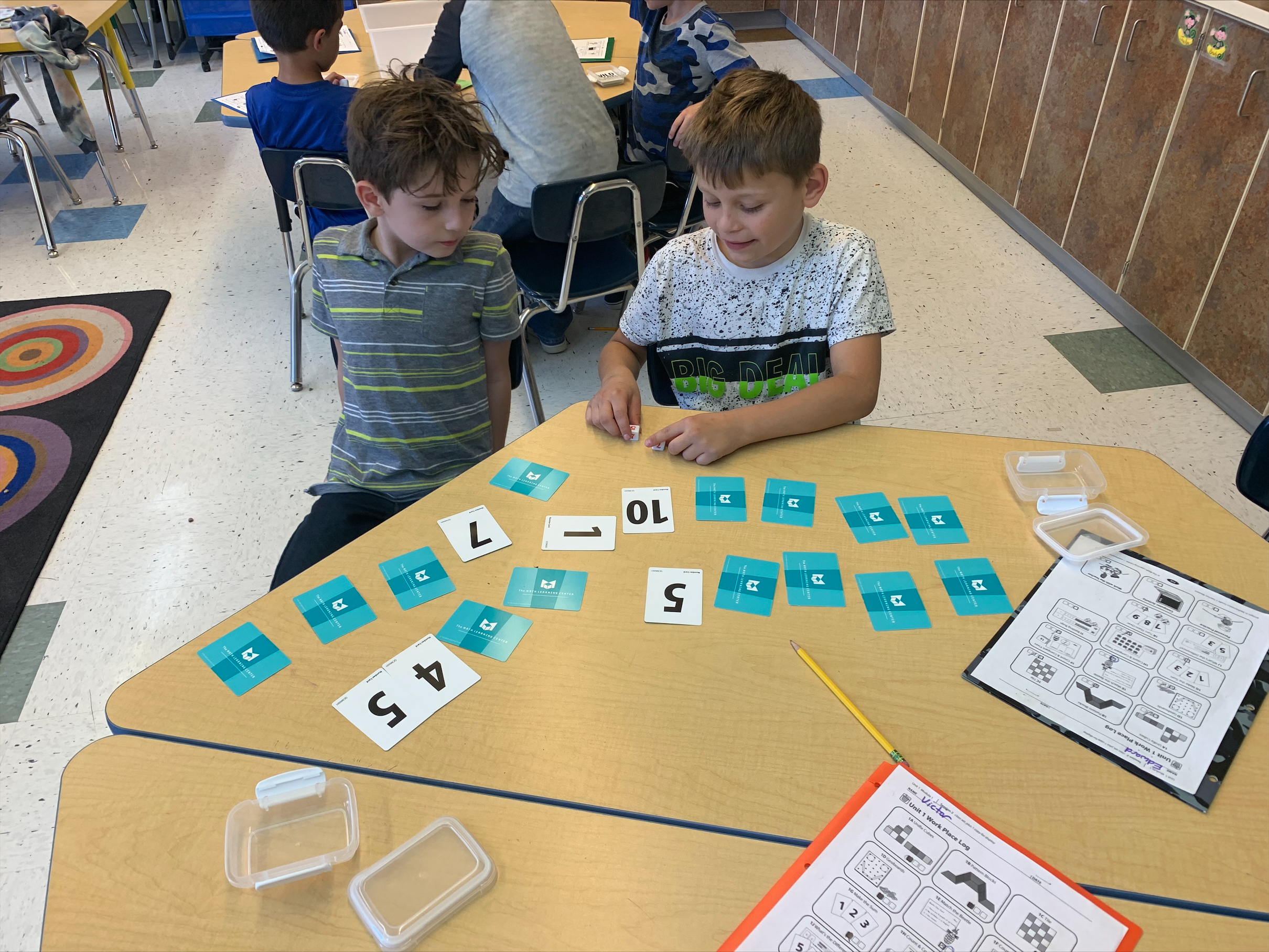 Two elementary students sit at a classroom table playing math games.
