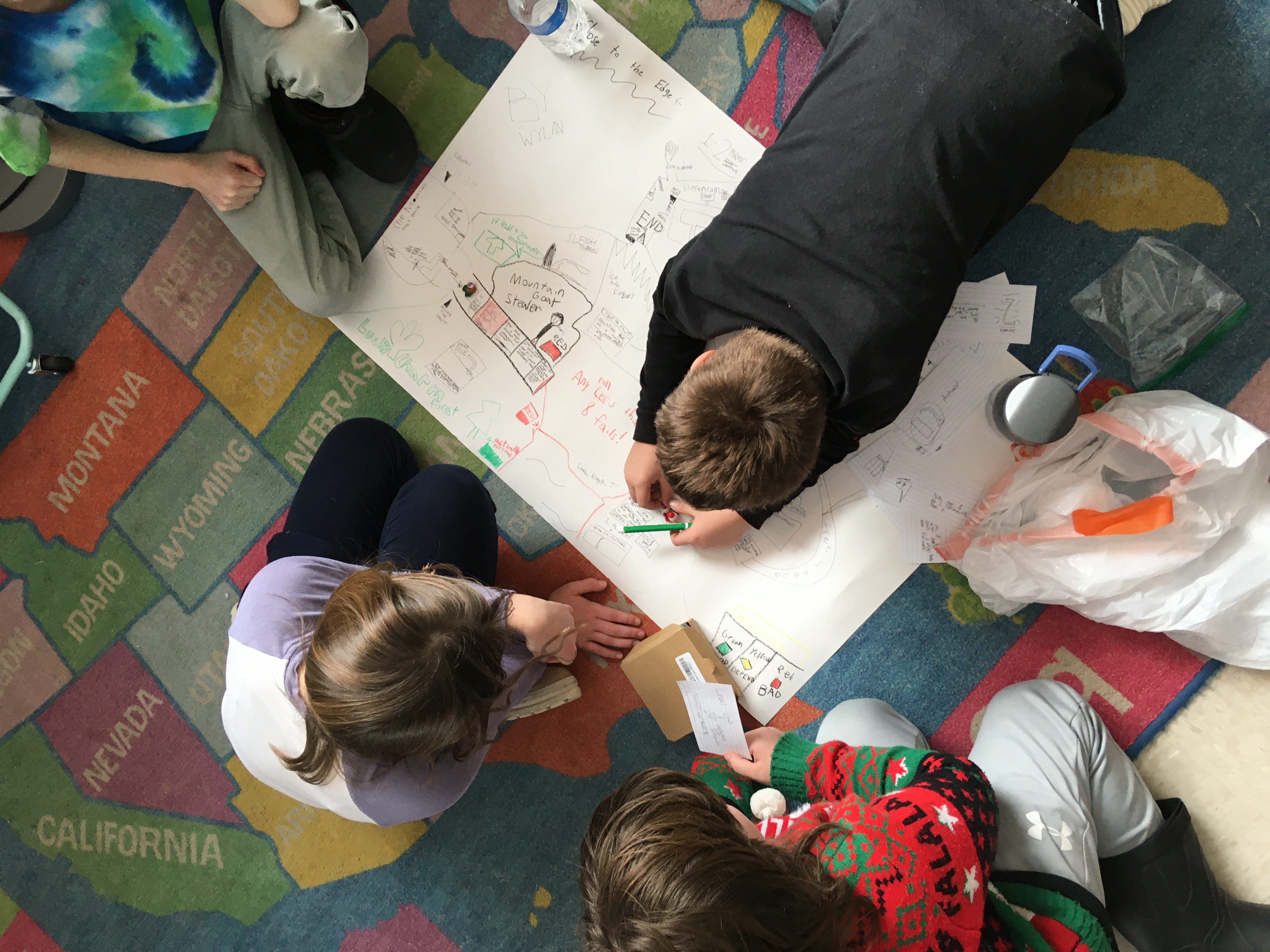 Four students pictured from above sit on the floor playing a student made board game.