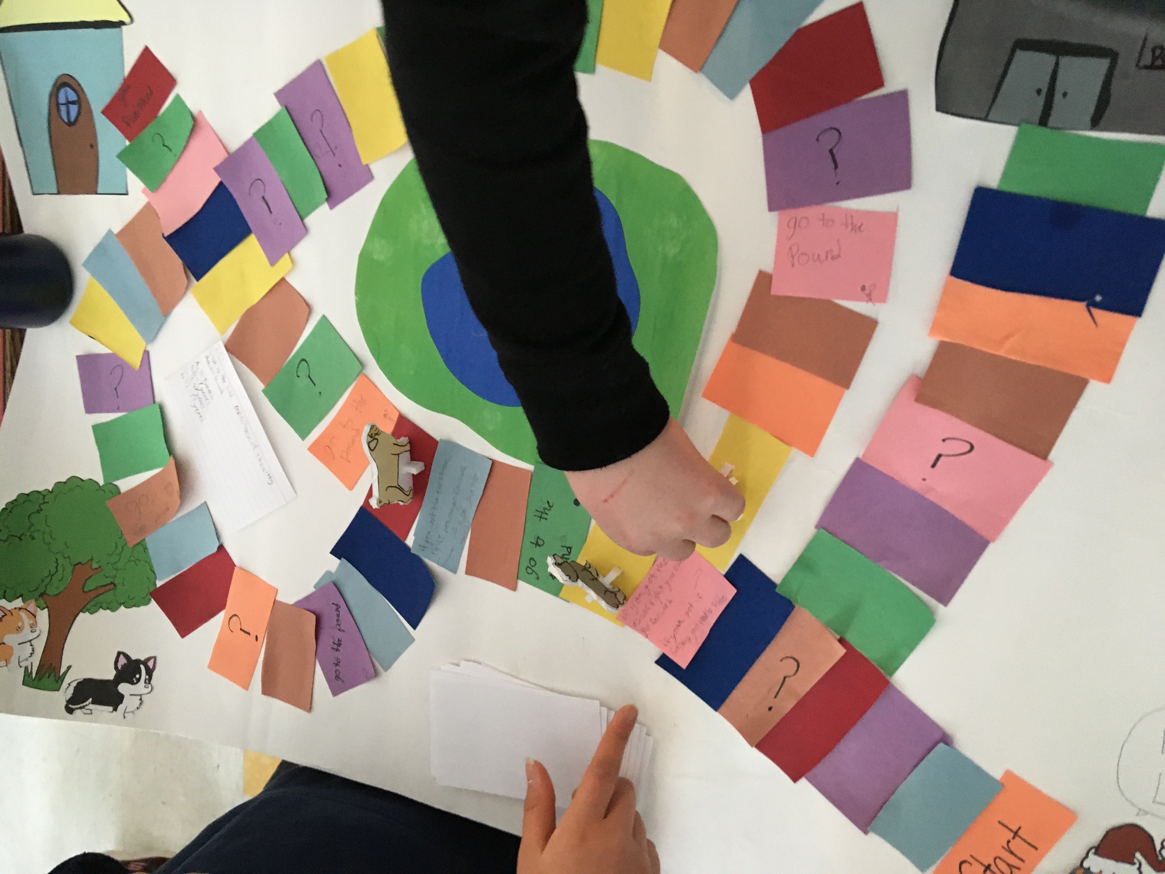 Student's hand shown as they play a colorful student made board game.
