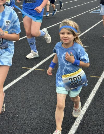 Young student dressed in blue t-shirt wearing blue headband and wristbands smile while running on the track.
