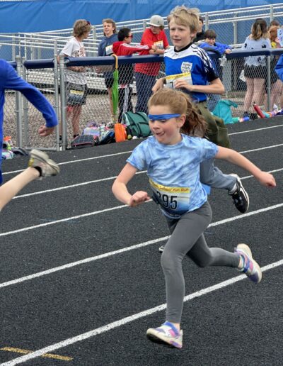 Two students running on the track while other students line the track in the background.