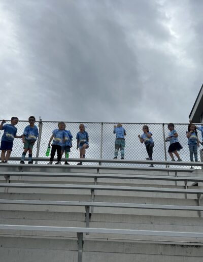 Twelve young students stand at the top of the empty bleachers on a cloudy day.