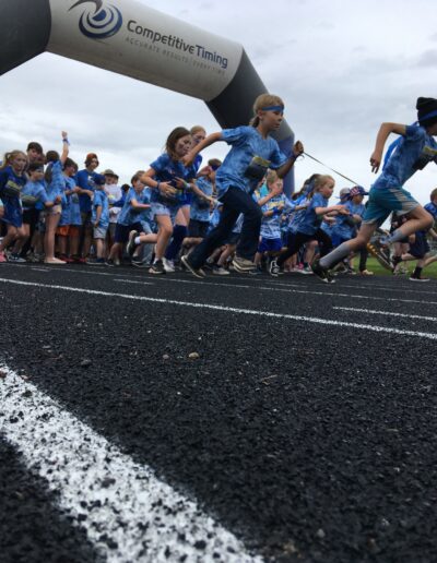 Students dressed in blue sprint out of the starting gate to run laps on the track.