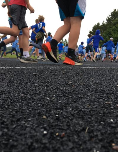 Closeup of the track and students legs and feet as they run laps on the track. In the background there are more students running.