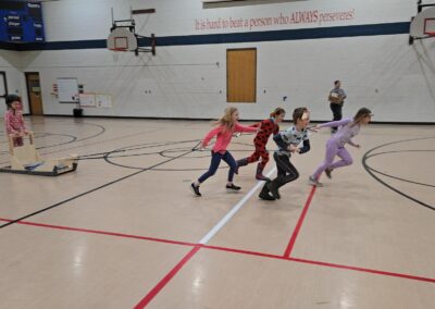 Students pretending they are sled dogs while pulling a sled across the gym.