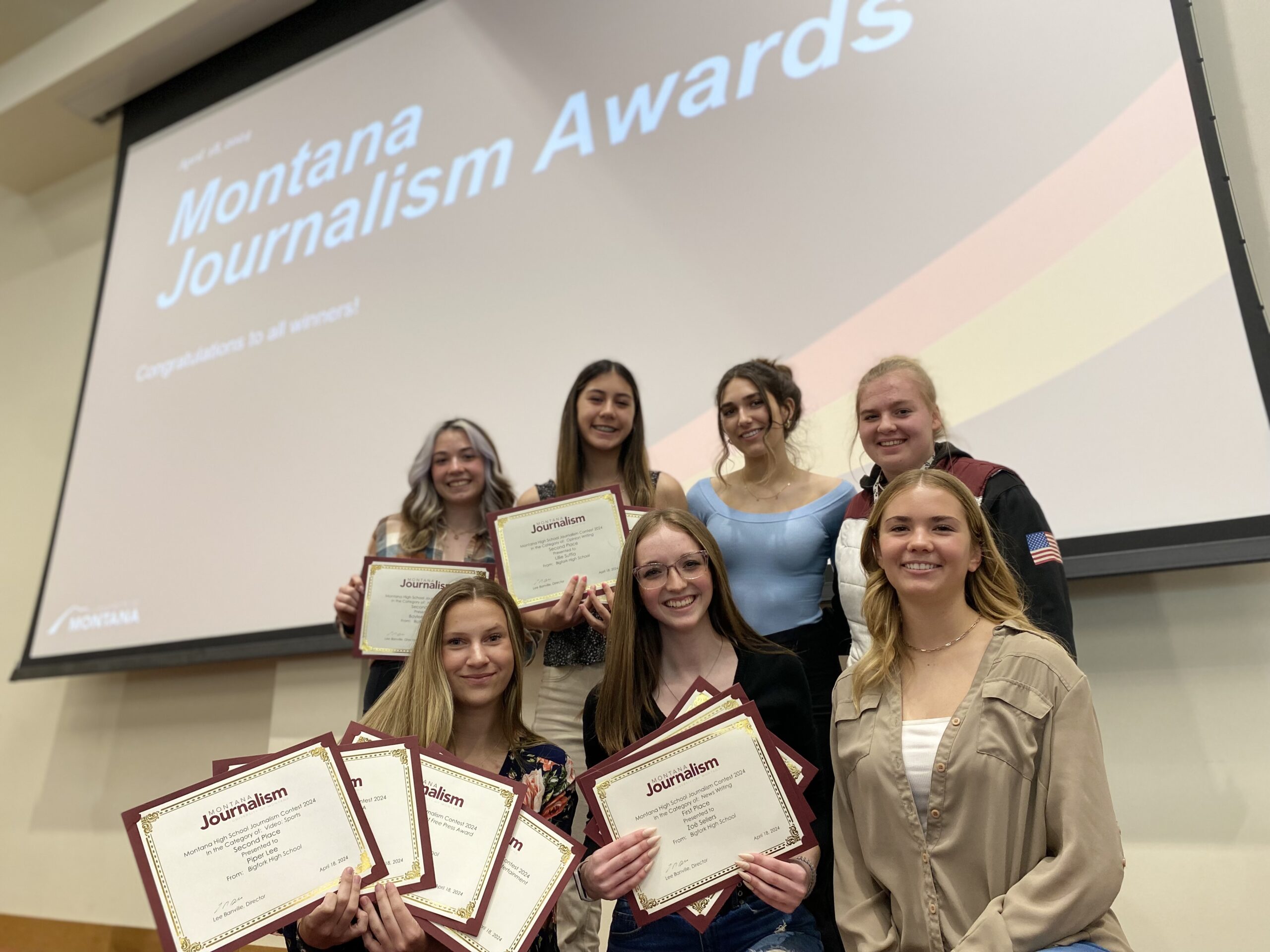 Journalism students holding their awards stand in front of presentation screen. 