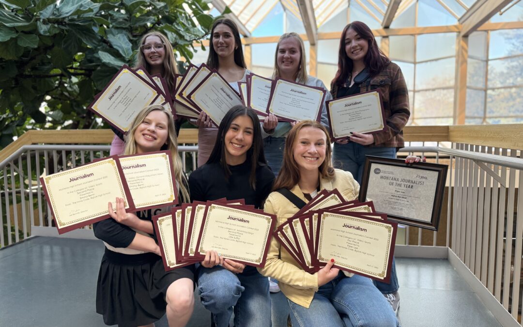 Bigfork journalism students pose with their awards and certificates in front of a bright glass wall.