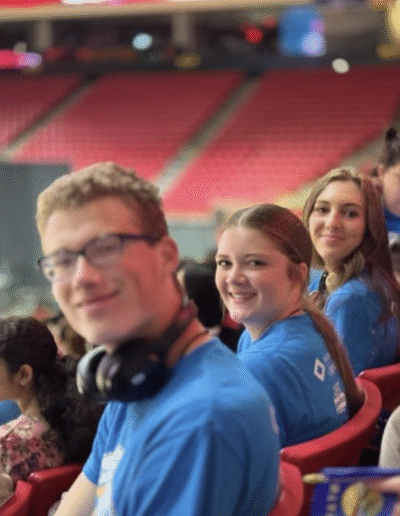 NHD students sit in the bleachers of a big stadium. The students smile while looking back over their shoulders.