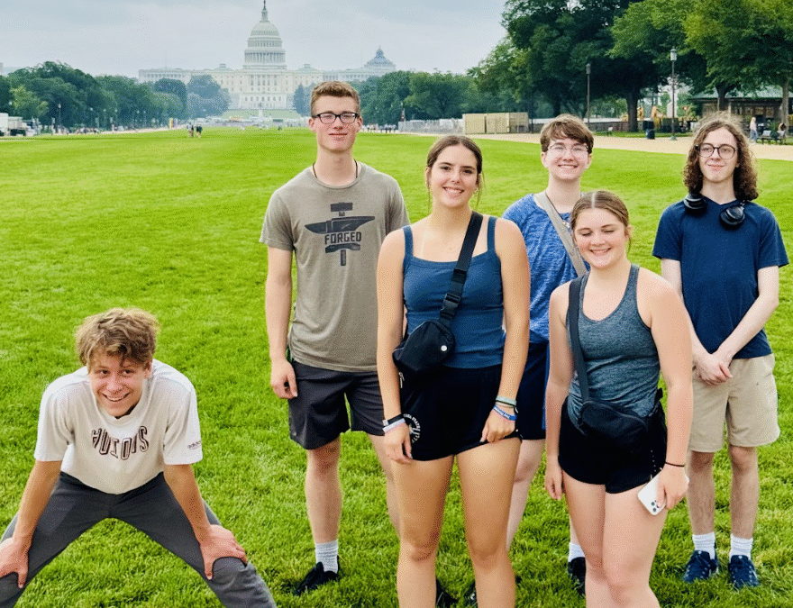 NHD students stand in the sun on a bright green lawn. In the background the U.S. Capitol building can be seen.