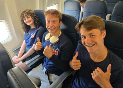 Three speech and Debate students in their plane seats giving thumbs up.