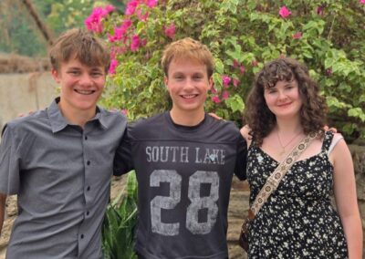 Three speech and debate students are standing in front of a lush plant with pink flowers.