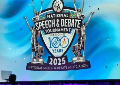 Logo of the National Speech and Debate tournament 2025 in Des Moines displayed on screen on a stage.