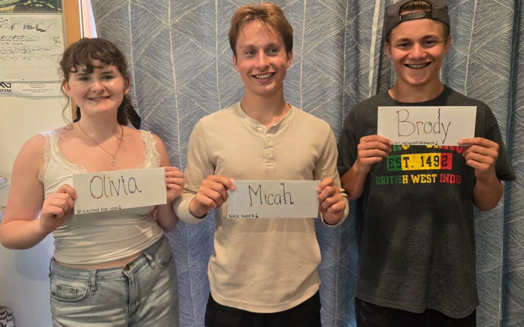 Olivia, Micah and Brody, Bigfork High School's speech and debate competitors are standing against a blue curtain holding up their name tags.