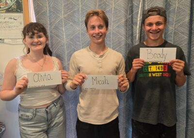 Olivia, Micah and Brody, Bigfork High School's speech and debate competitors are standing against a blue curtain holding up their name tags.