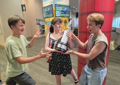 Three speech and debate students in the lobby of the competition venue pose with a trophy.