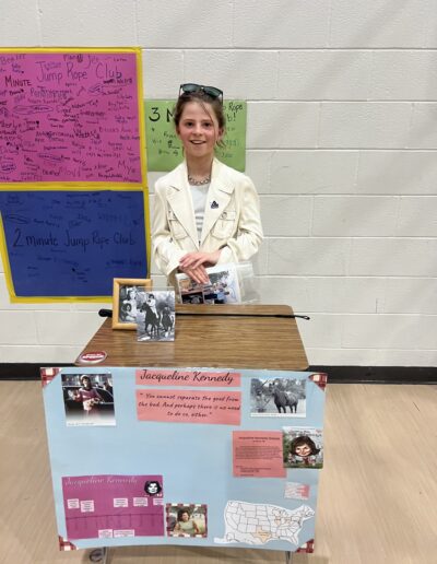 A student dressed up as Jacqueline Kennedy stands behind her Night of the Notables display.