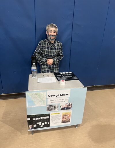 A student dressed up as George Lucas stands behind his Night of the Notables display.