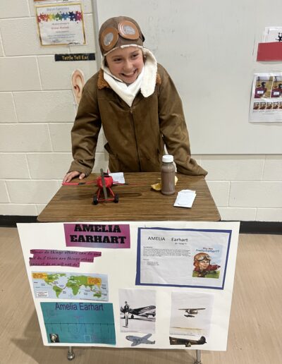 A student dressed up as Amelia Earhart stands behind her Night of the Notables display.