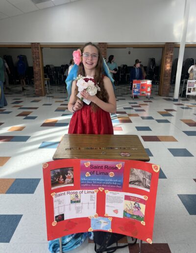 A student dressed up as Saint Rose of Lima stands behind her Night of the Notables display.