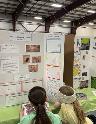 Two students are reading a book in front of a science fair display.