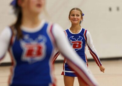 Two cheerleaders perform a cheer in a school gymnasium.