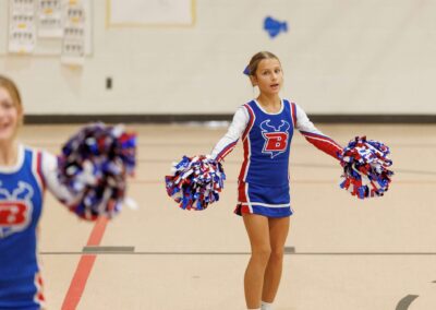 Two cheerleaders perform a cheer in a school gymnasium.