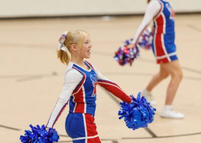 Two cheerleaders perform a cheer in a school gymnasium.
