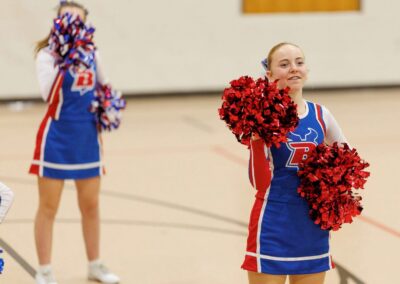 Two cheerleaders perform a cheer in a school gymnasium.